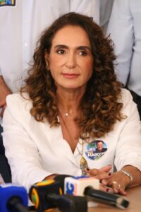 Mulher política em evento do Portal Balanço GO com microfones e apoiadores.